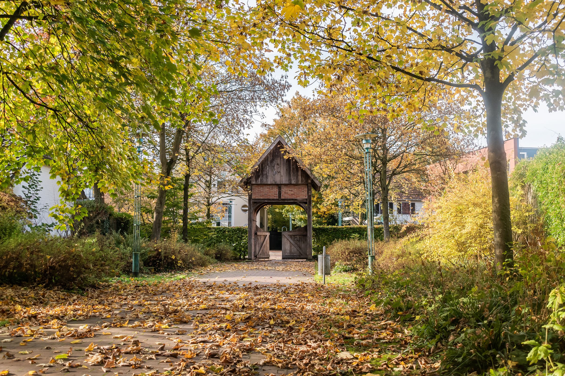 Ein hölzernes Tor am Museumsdorf Cloppenburg unter herbstlich gefärbten Bäumen.